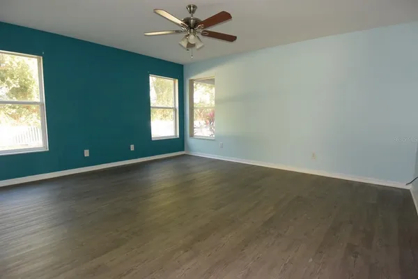 an empty room with wooden floor fan and windows