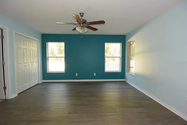 an empty room with wooden floor fan and windows