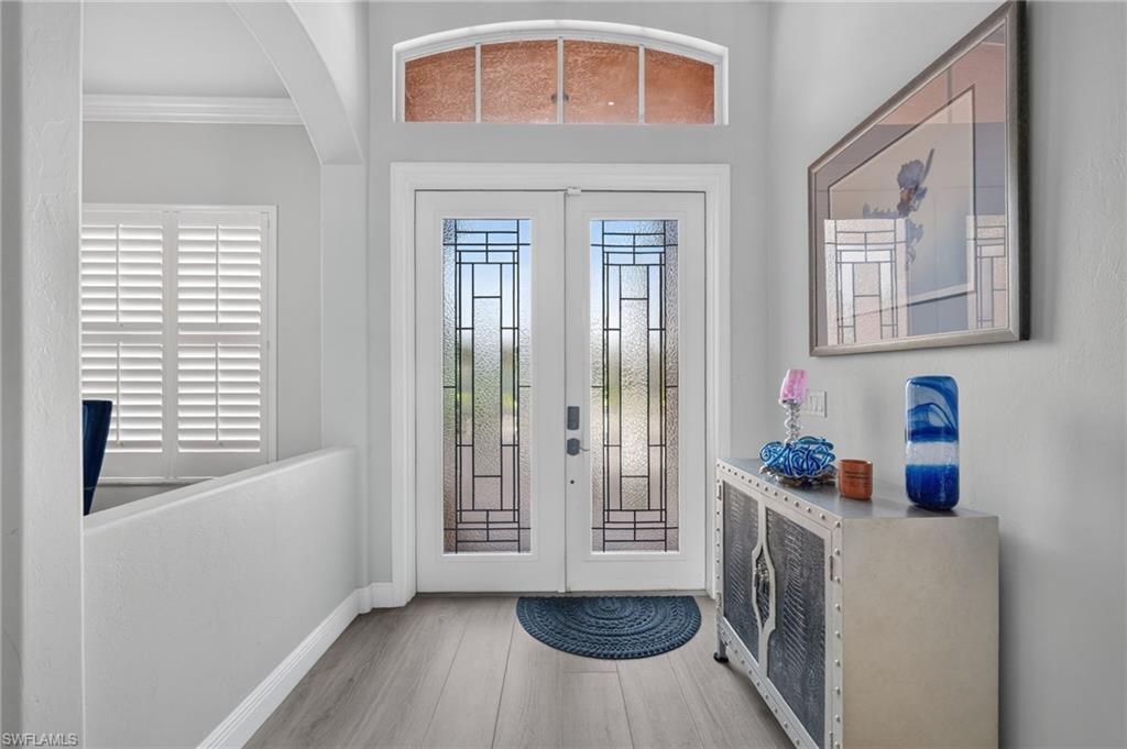 9970 Rookery Circle Estero, FL 33928 - Photo 5 of 50 Double-door entry with decorative glass inserts and transom window, light wood-finish flooring, and crown molding