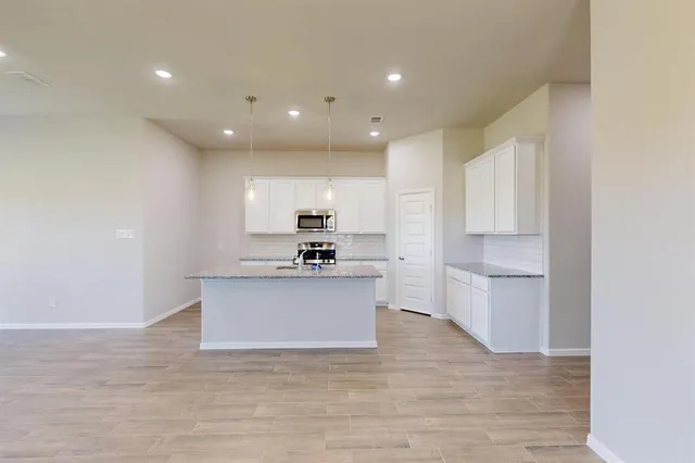 a kitchen with stainless steel appliances granite countertop a refrigerator a sink dishwasher a stove and a dining table with wooden floor