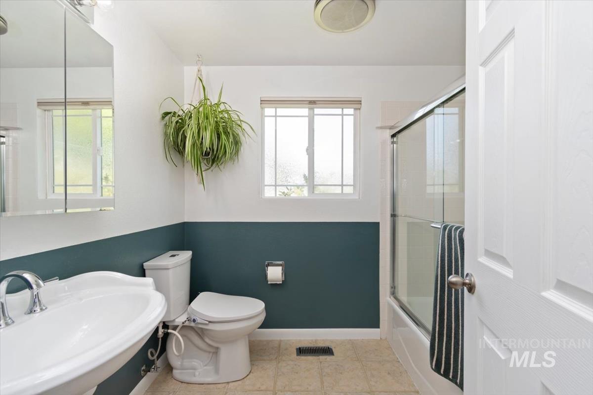 10178 West Fox Ridge Drive Boise, ID 83709 - Photo 15 of 36 Bathroom featuring a built-in shower-over-tub with glass enclosure, white pedestal sink, and two windows with privacy blinds