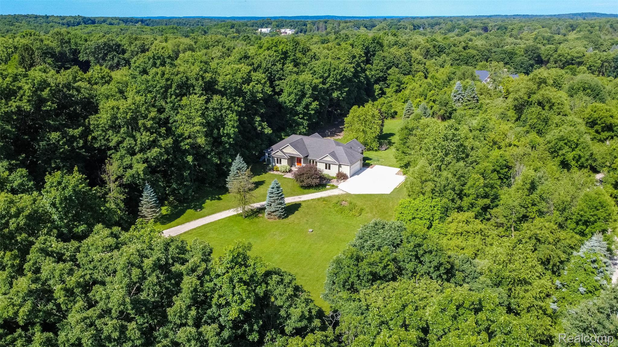 9887 Hadley Road Clarkston, MI 48348 - Photo 43 of 56 Single-story residence set amidst dense woodlands, featuring a light-toned exterior, dark roof, and an attached two-car garage