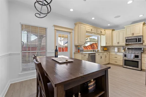 a kitchen with stainless steel appliances granite countertop a stove a refrigerator a kitchen island a dining table and chairs with wooden floor