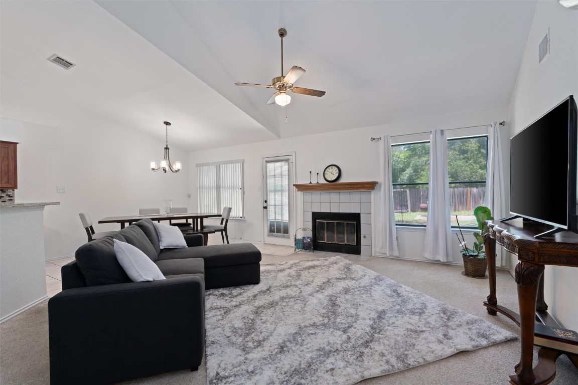 Living area with vaulted ceiling, ceiling fan, plenty of natural light, a chandelier, and light colored carpet