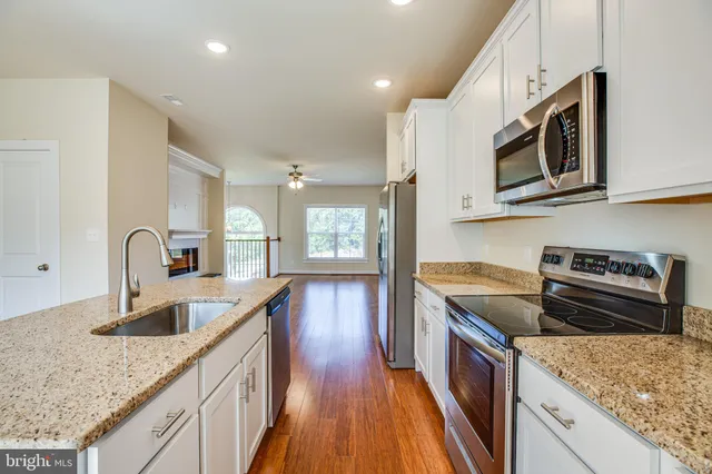 a kitchen with wooden floors white cabinets appliances and a window