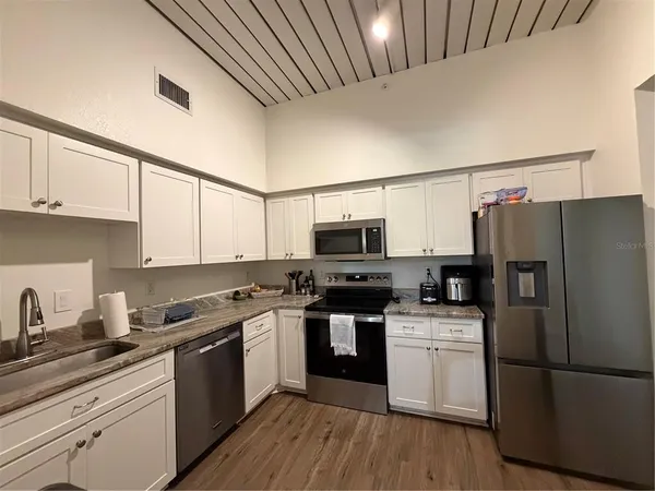 a kitchen with stainless steel appliances a refrigerator stove a sink and white cabinets