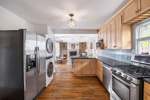 a kitchen with stainless steel appliances granite countertop a refrigerator a sink dishwasher a stove and a dining table with wooden floor