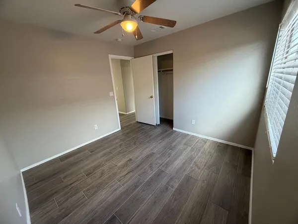 an empty room with wooden floor fan and windows
