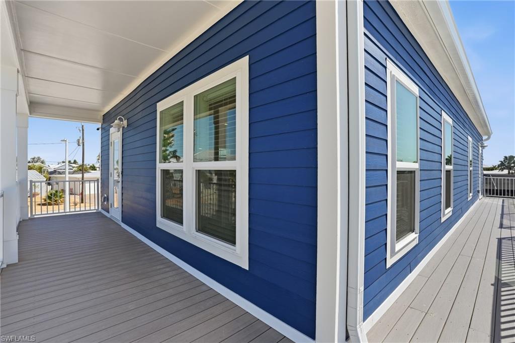 1 Fairview Boulevard Fort Myers Beach, FL 33931 - Photo 39 of 48 Exterior featuring blue horizontal siding, multiple windows with white trim, a covered porch with white columns, and gray decking - Virtually Edited Image