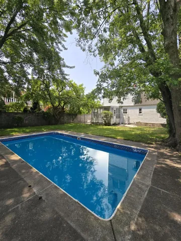 a view of swimming pool with seating space and trees in the background