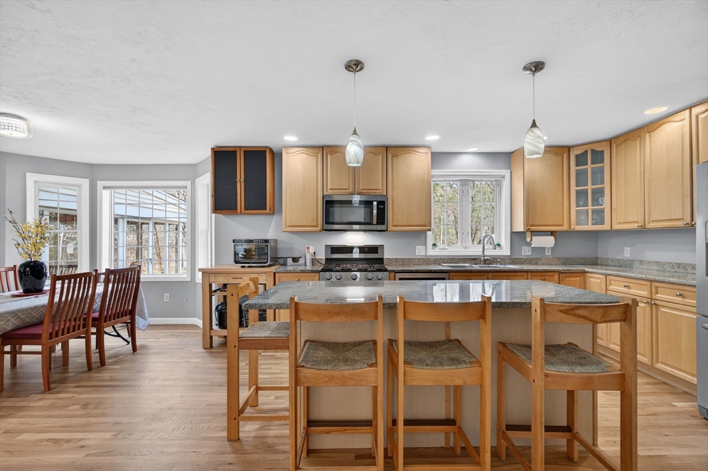 155 Brook Street Hudson, MA 01749 - Photo 3 of 42 a large kitchen with granite countertop a stove a sink a dining table and chairs with wooden floor