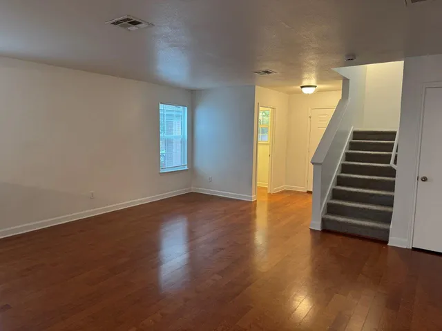 a view of an empty room with wooden floor and stairs
