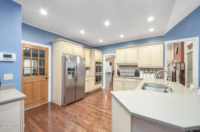 a large kitchen with kitchen island a large window cabinets a sink and stainless steel appliances