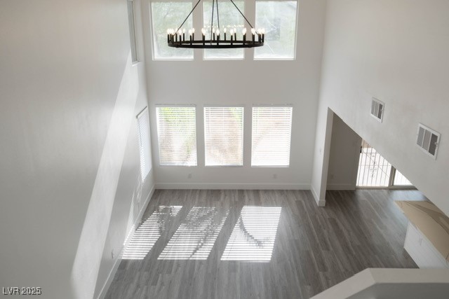 Unfurnished living room featuring visible vents, baseboards, a towering ceiling, and a chandelier