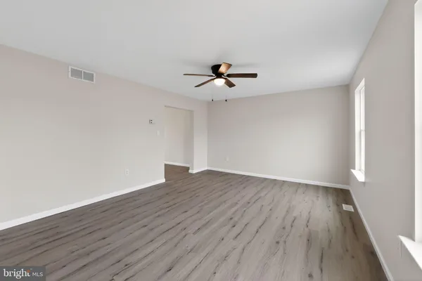 a view of an empty room with wooden floor and a ceiling fan
