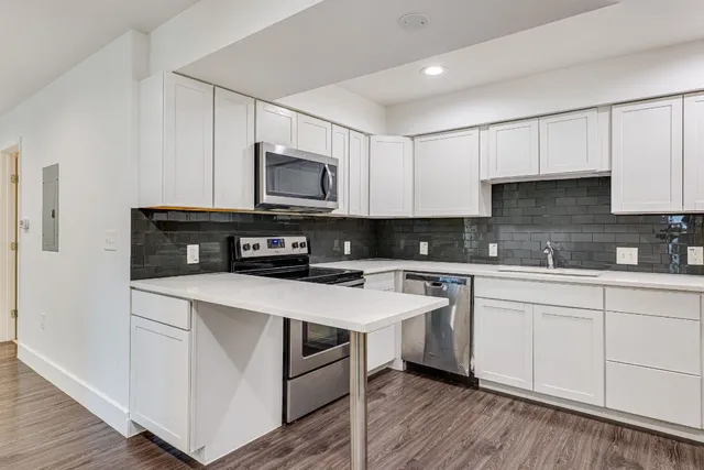 a kitchen with stainless steel appliances granite countertop a stove top oven a sink and white cabinets