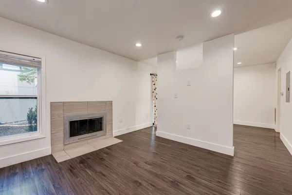 a view of an empty room with wooden floor fireplace and a window