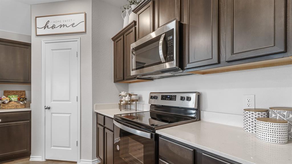 1667 Mantle Road Crandall, TX 75114 - Photo 3 of 20 Contemporary kitchen featuring dark wood cabinetry, light-toned countertops, and a full suite of stainless steel appliances including a built-in microwave and electric range