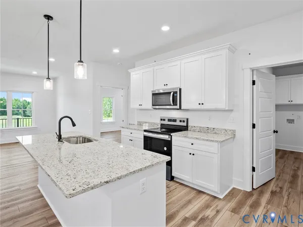a kitchen with stainless steel appliances granite countertop a sink a stove a refrigerator and white cabinets with wooden floor