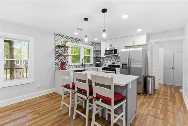 a kitchen with stainless steel appliances kitchen island granite countertop a refrigerator a sink a stove and white cabinets with wooden floor