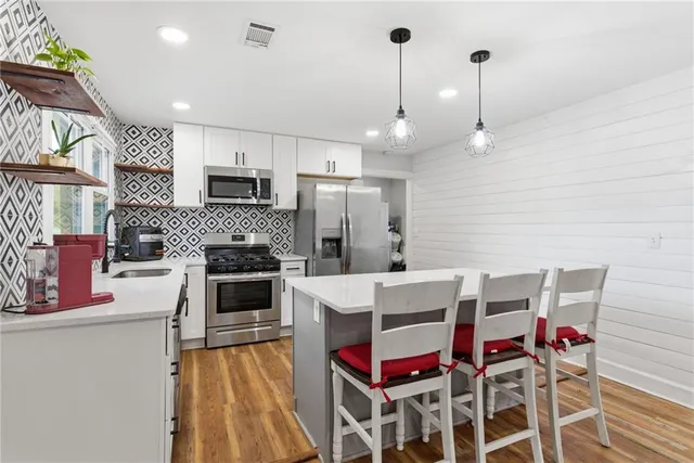 a kitchen with stainless steel appliances kitchen island granite countertop a stove a sink dishwasher and a refrigerator with wooden floor