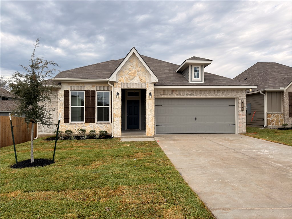 View of front of house featuring stone siding, driveway, an attached garage, roof with shingles, and brick siding