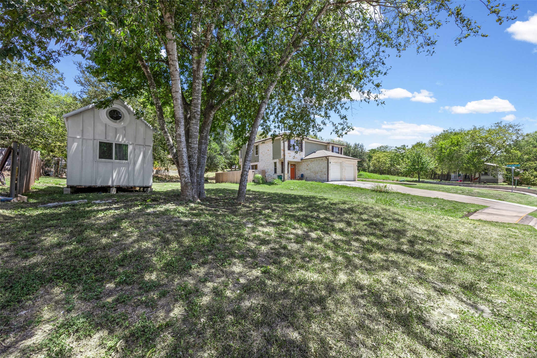 5706 Spring Meadow Road Austin, TX 78744 - Photo 3 of 11 Mature trees shade the grassy yard leading to a detached outbuilding and stone-accented home.