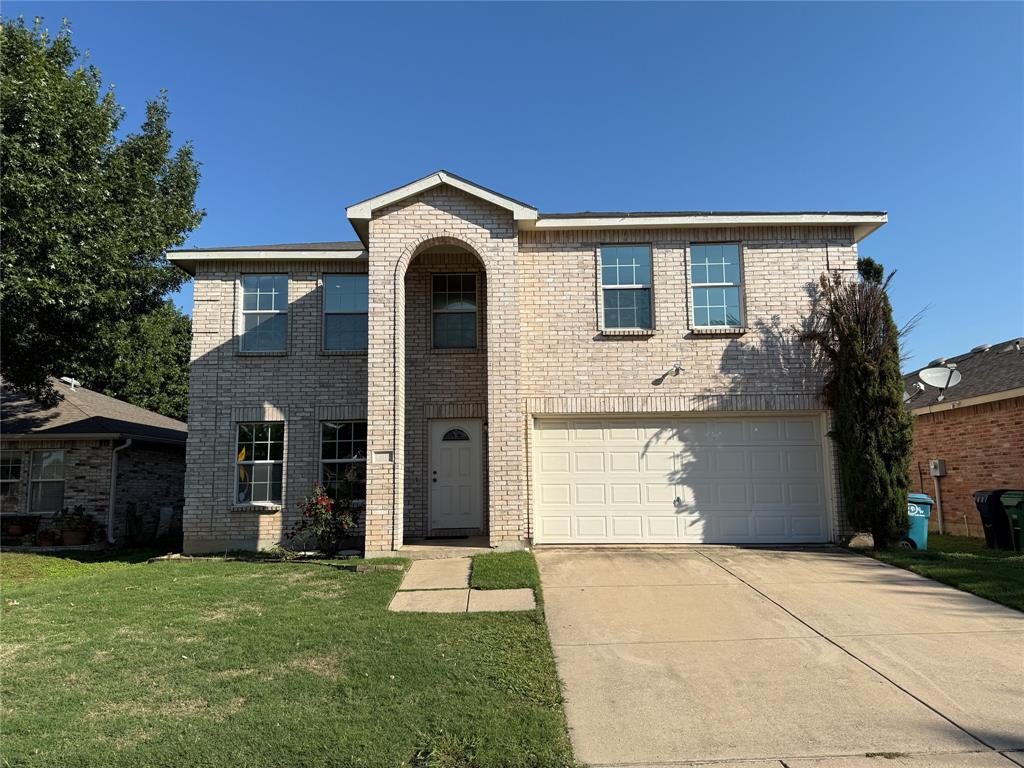 Traditional home featuring an attached garage, concrete driveway, a front lawn, and brick siding