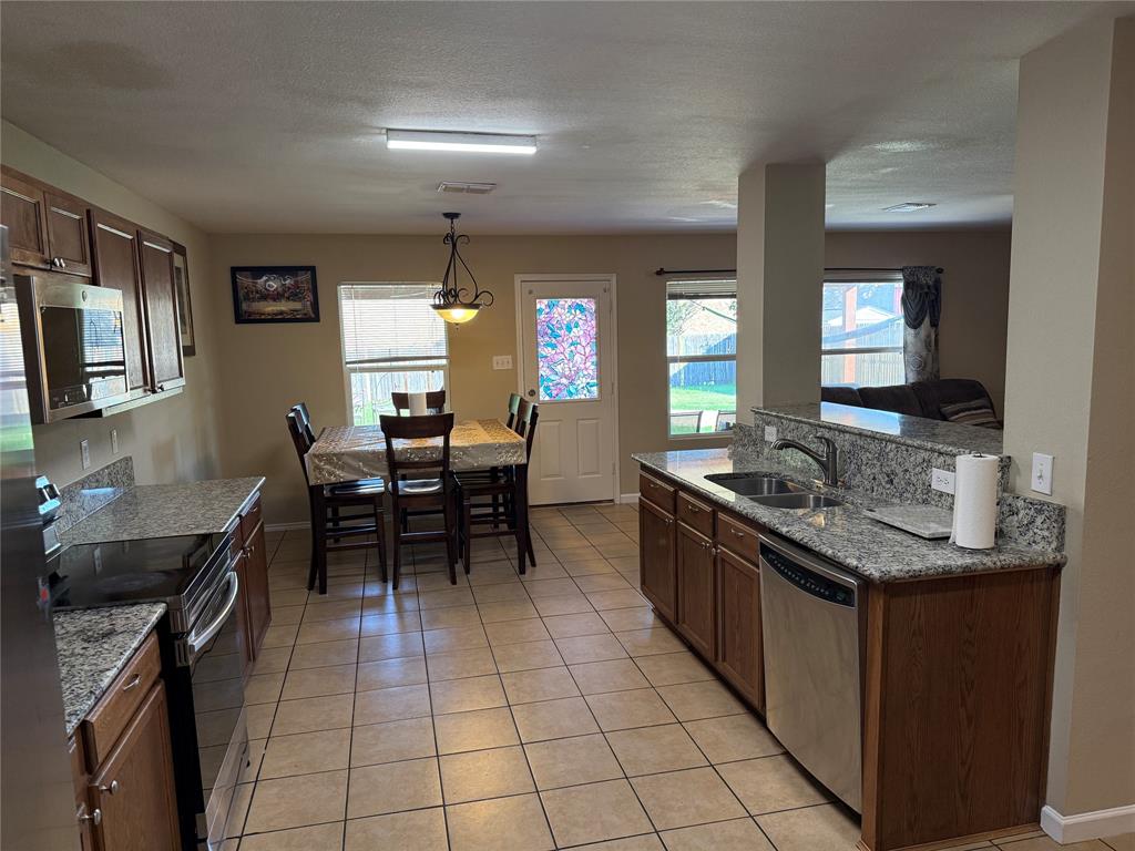 5718 Green Ivy Road Denton, TX 76210 - Photo 6 of 23 Kitchen featuring stainless steel appliances, pendant lighting, light tile patterned flooring, light stone countertops, and a textured ceiling