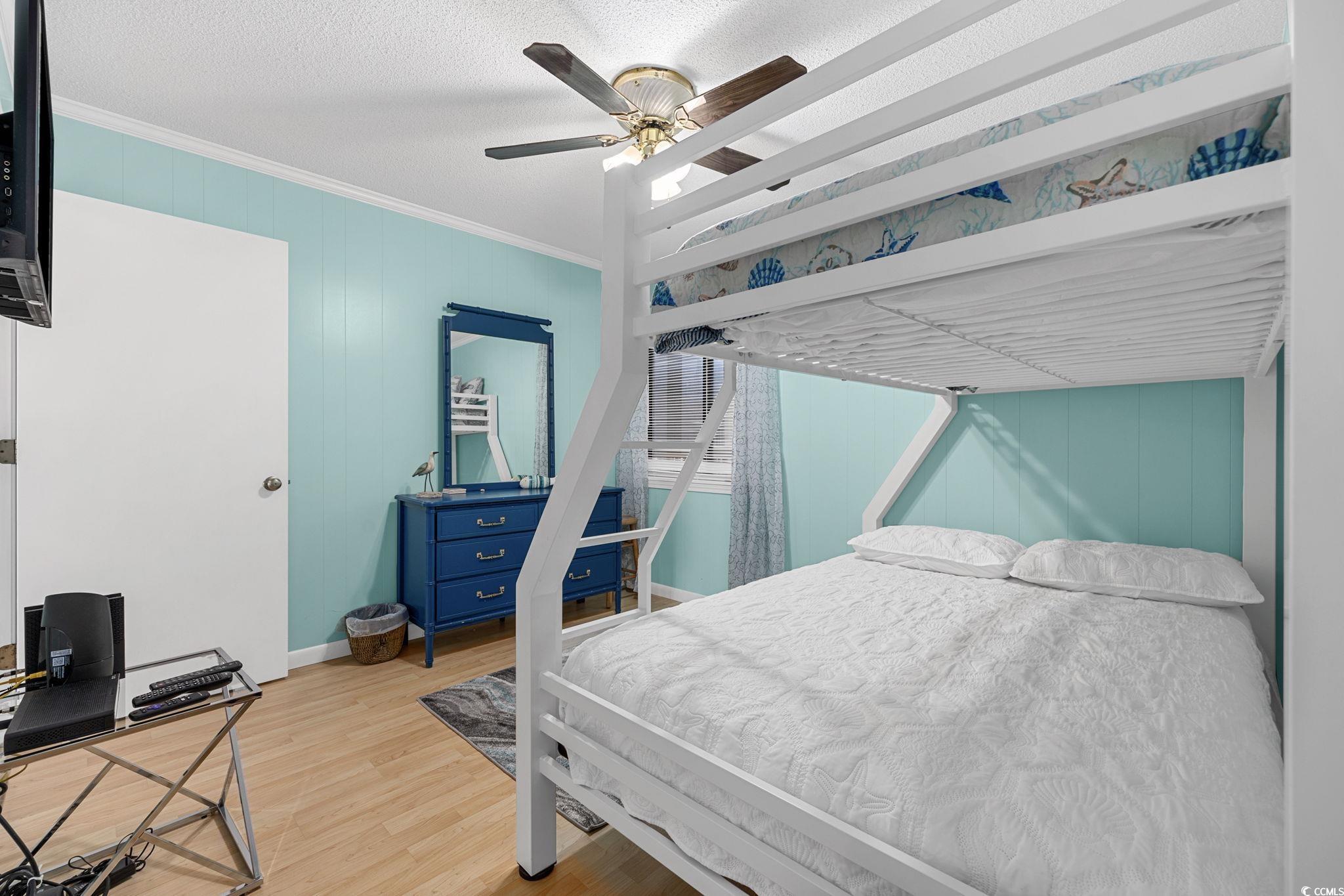 191 Maison Drive, Unit B312 Myrtle Beach, SC 29572 - Photo 29 of 40 Bedroom featuring ornamental molding, light wood-style flooring, ceiling fan, wooden walls, and a textured ceiling