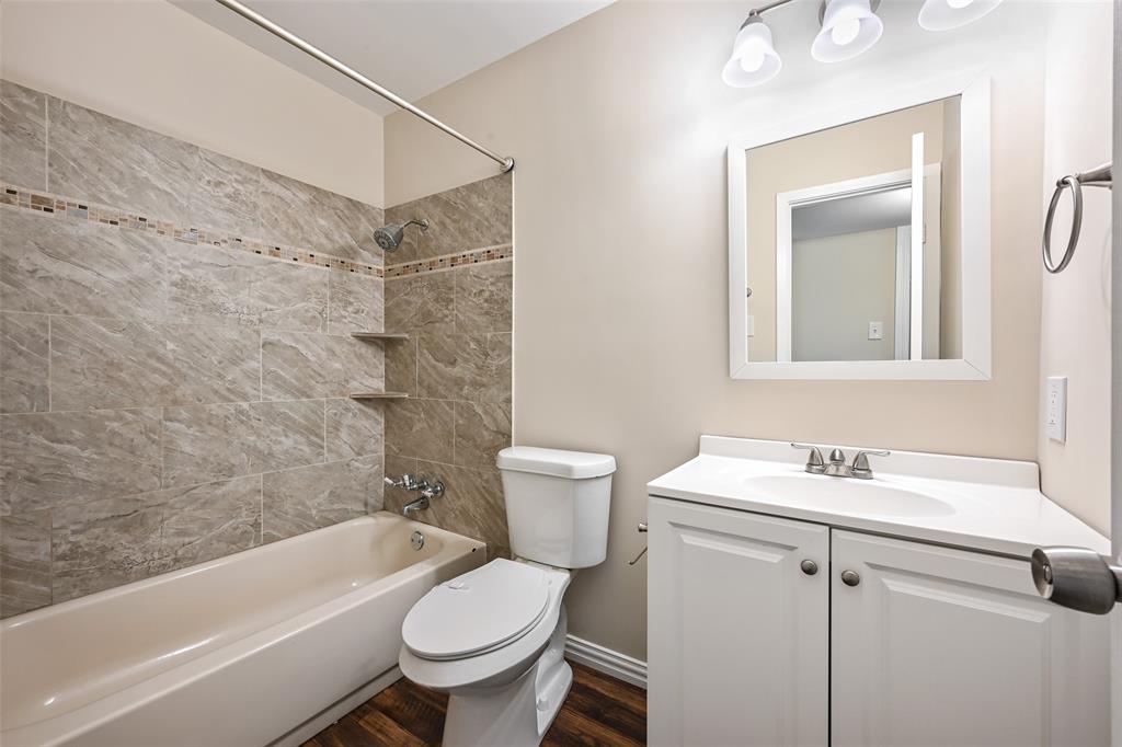 7318 Emory Oak Lane Dallas, TX 75249 - Photo 18 of 28 Bathroom featuring a ceramic tile tub surround with mosaic accent, built-in shower shelves, wood-finish flooring, white vanity with integrated sink, and framed mirror