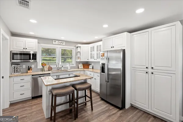 a kitchen with stainless steel appliances granite countertop a refrigerator a stove a sink and white cabinets with wooden floor