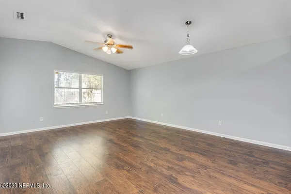 an empty room with wooden floor ceiling fan and windows