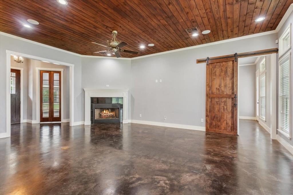 259 County Road 149 Riesel, TX 76682 - Photo 6 of 40 Unfurnished living room with a barn door, wood ceiling, finished concrete floors, ornamental molding, and a tiled fireplace