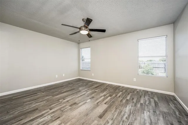 an empty room with wooden floor fan and windows