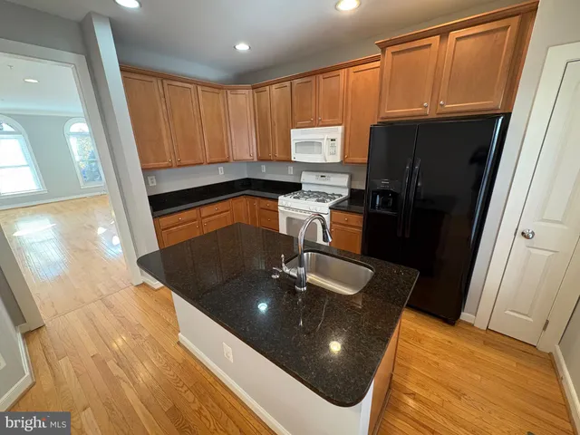 a kitchen with stainless steel appliances granite countertop a refrigerator a sink a stove white cabinets and wooden floor