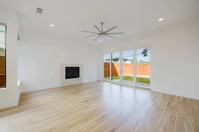 an empty room with wooden floor chandelier fan and windows