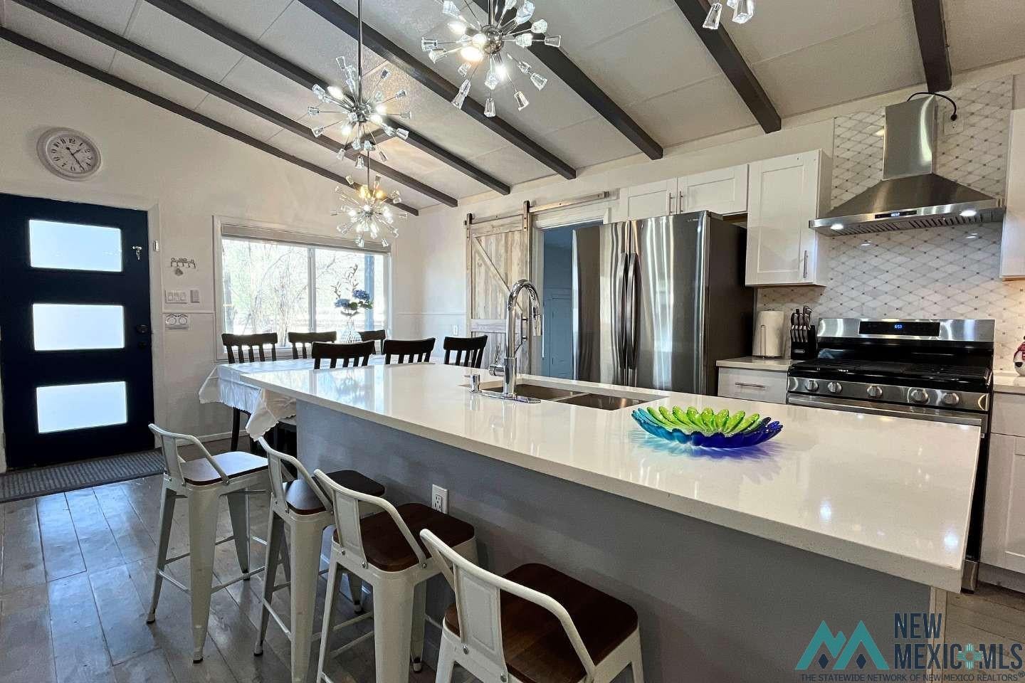 241 Junction Road Ruidoso, NM 88345 - Photo 7 of 44 Kitchen with tasteful backsplash, a barn door, dark wood finished floors, wall chimney range hood, and stainless steel appliances