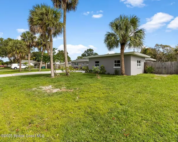 a white house with a big yard and palm trees