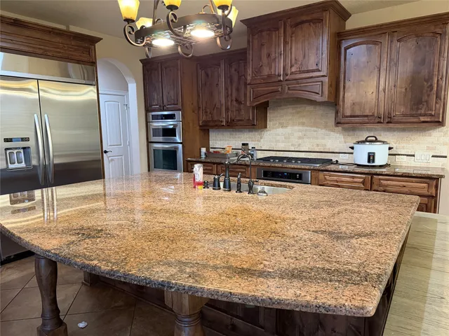a kitchen with kitchen island granite countertop wooden cabinets refrigerator and stove