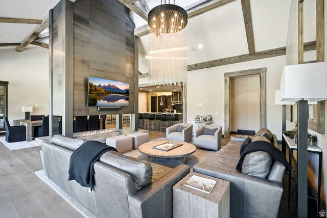 1575 Old Ranch Road Park City, UT 84098 - Photo 7 of 45 Vaulted ceilings with exposed beams, a floor-to-ceiling fireplace with integrated television, wood-finish flooring, and a contemporary chandelier