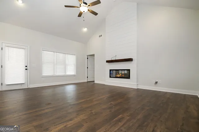 an empty room with wooden floor chandelier fan and windows