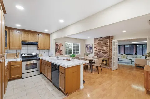 a kitchen with stainless steel appliances granite countertop a stove top oven a sink dishwasher a dining table and chairs with wooden floor