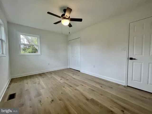 an empty room with wooden floor ceiling fan and windows