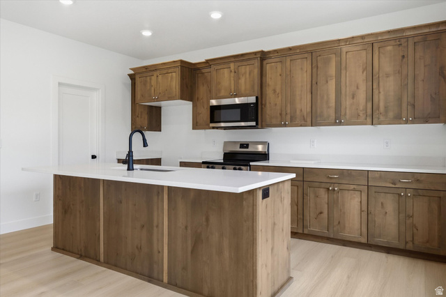 844 North 400 West Logan, UT 84321 - Photo 11 of 43 Kitchen featuring an expansive island with a matte black faucet, wood-finish cabinetry, stainless steel appliances, and light-toned flooring