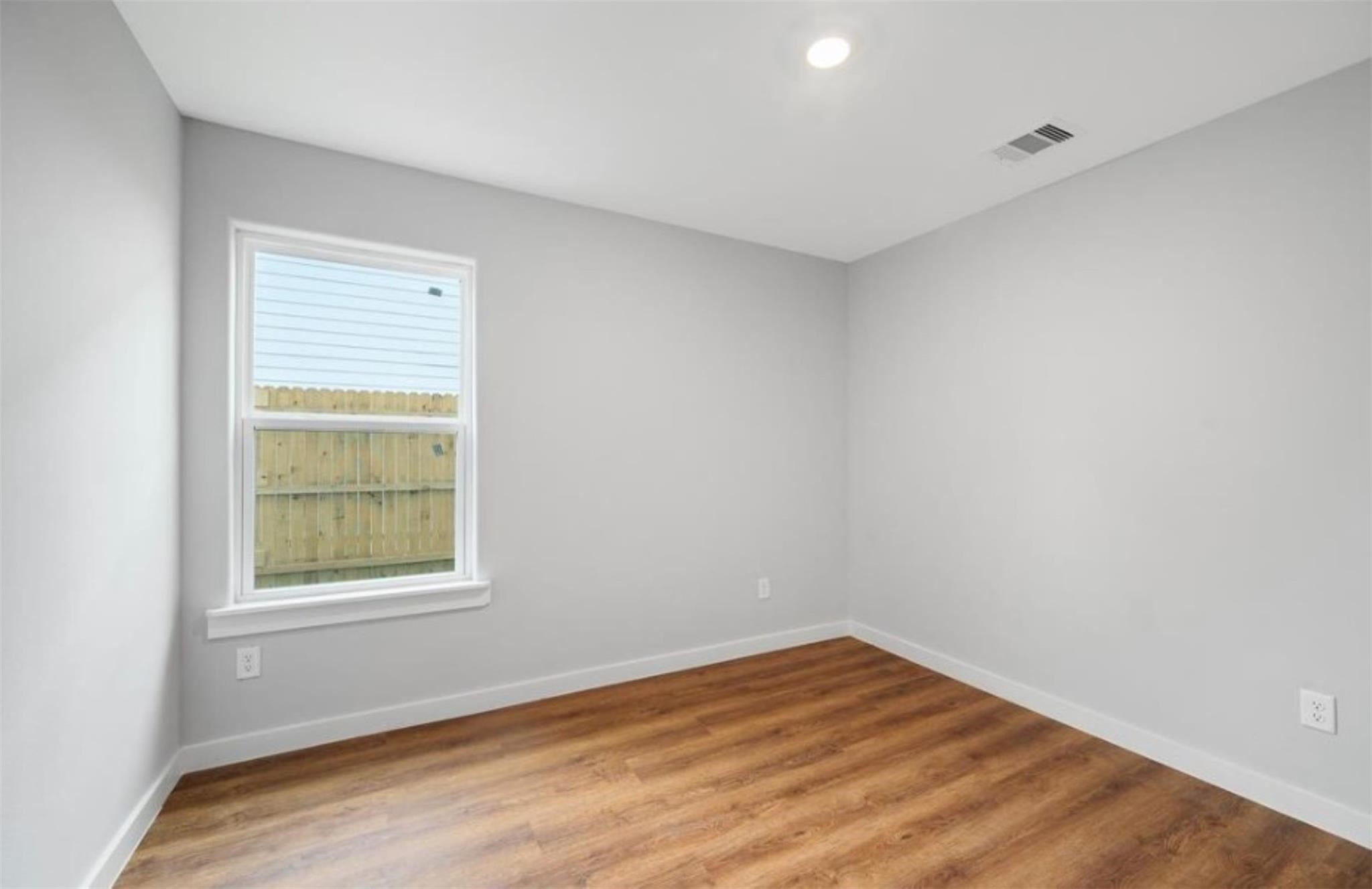 8120 Laura Koppe Road, Unit B Houston, TX 77028 - Photo 12 of 25 This room features fresh gray walls and warm wood flooring, creating a cozy atmosphere. A large window allows natural light, and there’s a ceiling light for evening brightness. Ideal for a bedroom or home office.