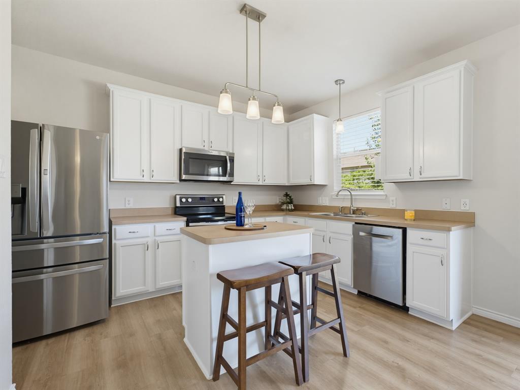 13268 Fencerow Road Fort Worth, TX 76244 - Photo 3 of 25 Bright kitchen featuring a central island, white cabinetry, stainless steel appliances, wood-finish flooring, and a large window