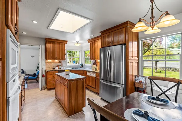 a kitchen with stainless steel appliances granite countertop a refrigerator a sink dishwasher a stove and a dining table next to a window