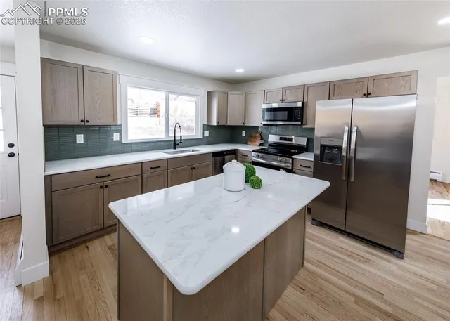 a kitchen with stainless steel appliances granite countertop a sink a stove a refrigerator a center island and wooden floor