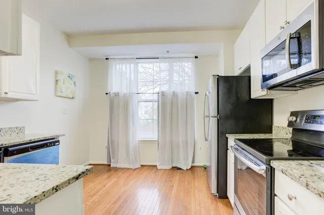 a kitchen with stainless steel appliances granite countertop a refrigerator a stove and a sink with wooden floors